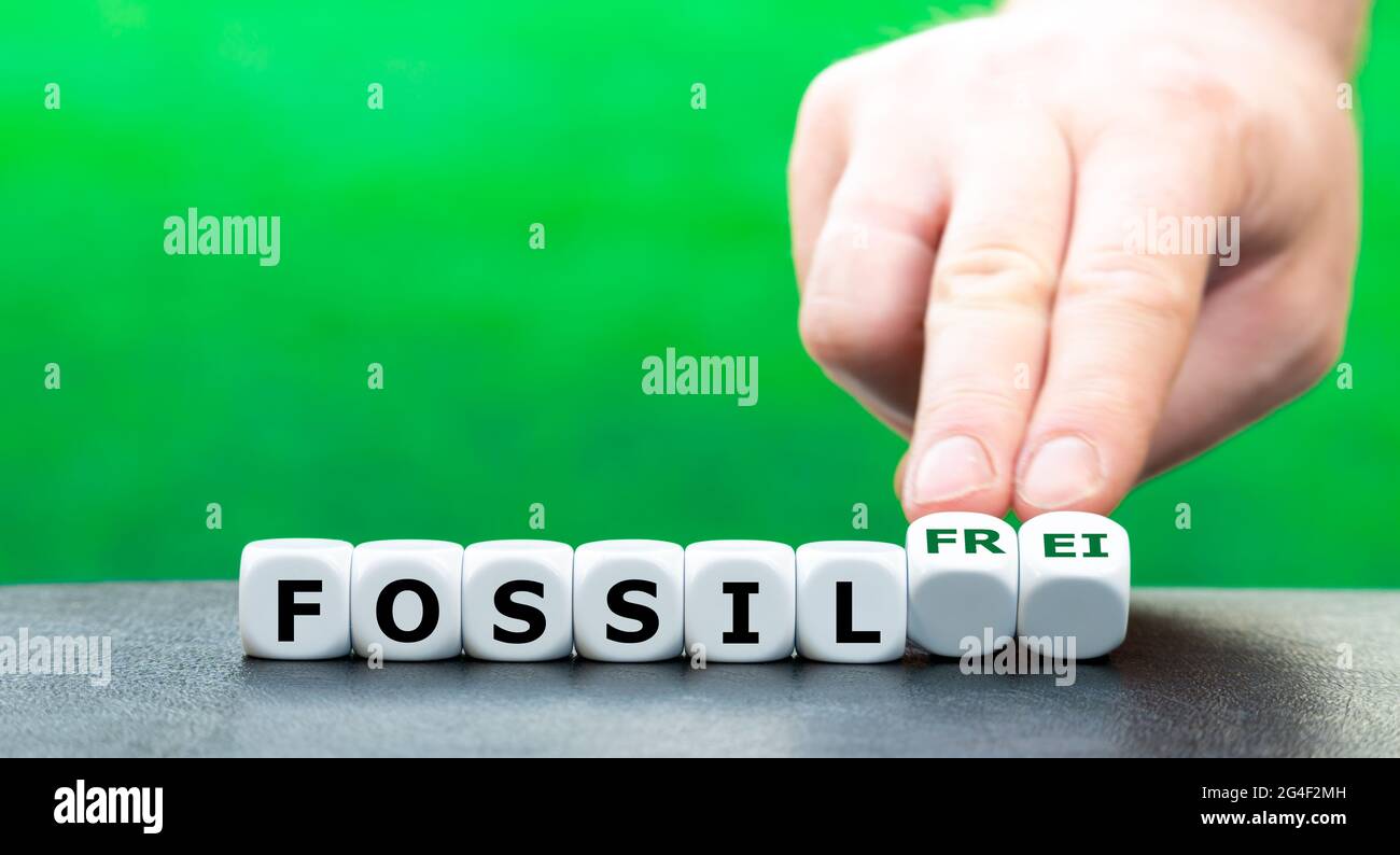 Hand dreht Würfel und ändert den deutschen Ausdruck 'fossil' (fossil) in 'fossil frei' (fossil frei). Stockfoto