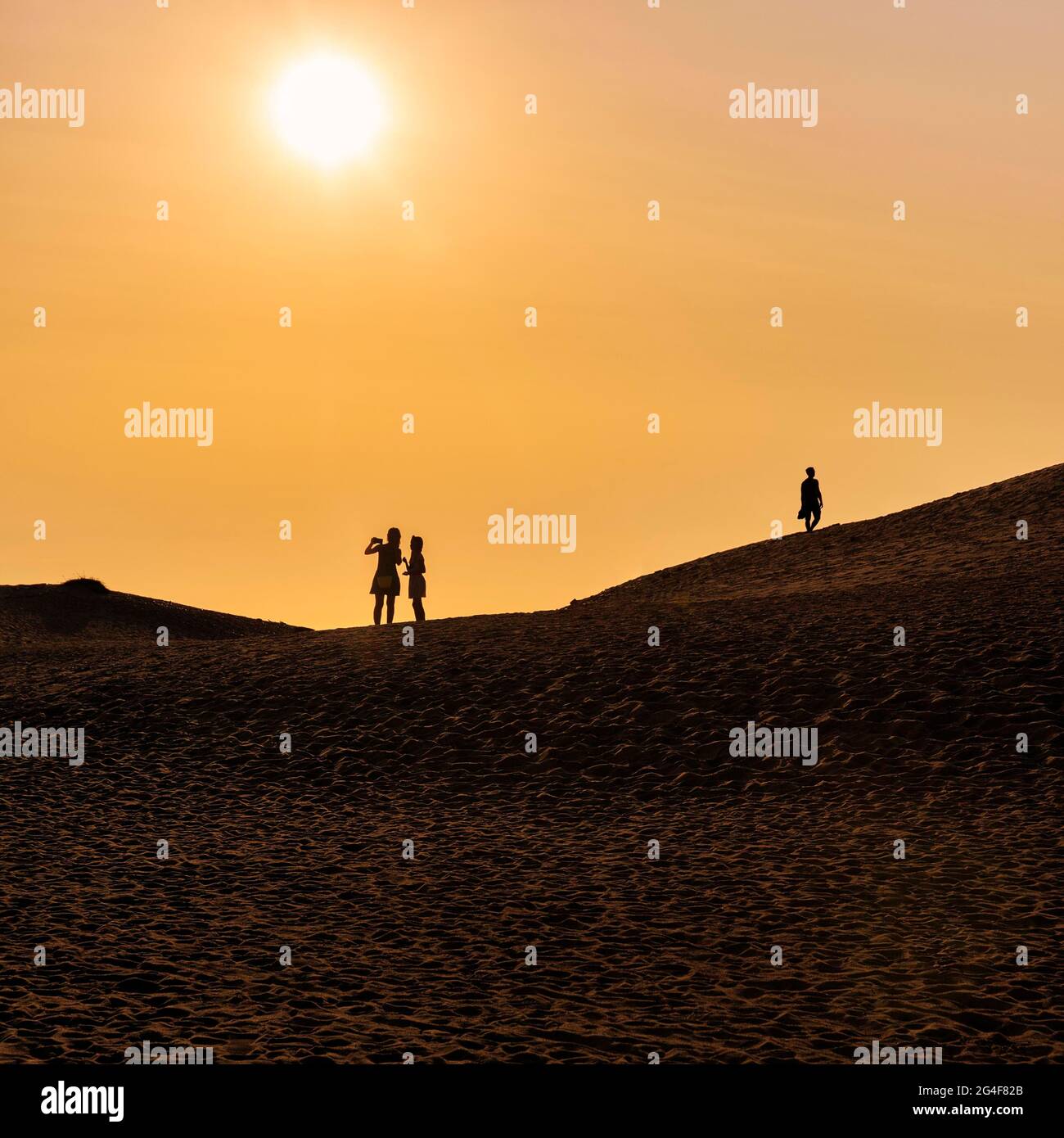 Drei Menschen auf der Düne, zwei Frauen, die Selfie machen, Mann, der läuft, Silhouetten bei Sonnenuntergang, Nordjylland, Nordjütland, Dänemark Stockfoto