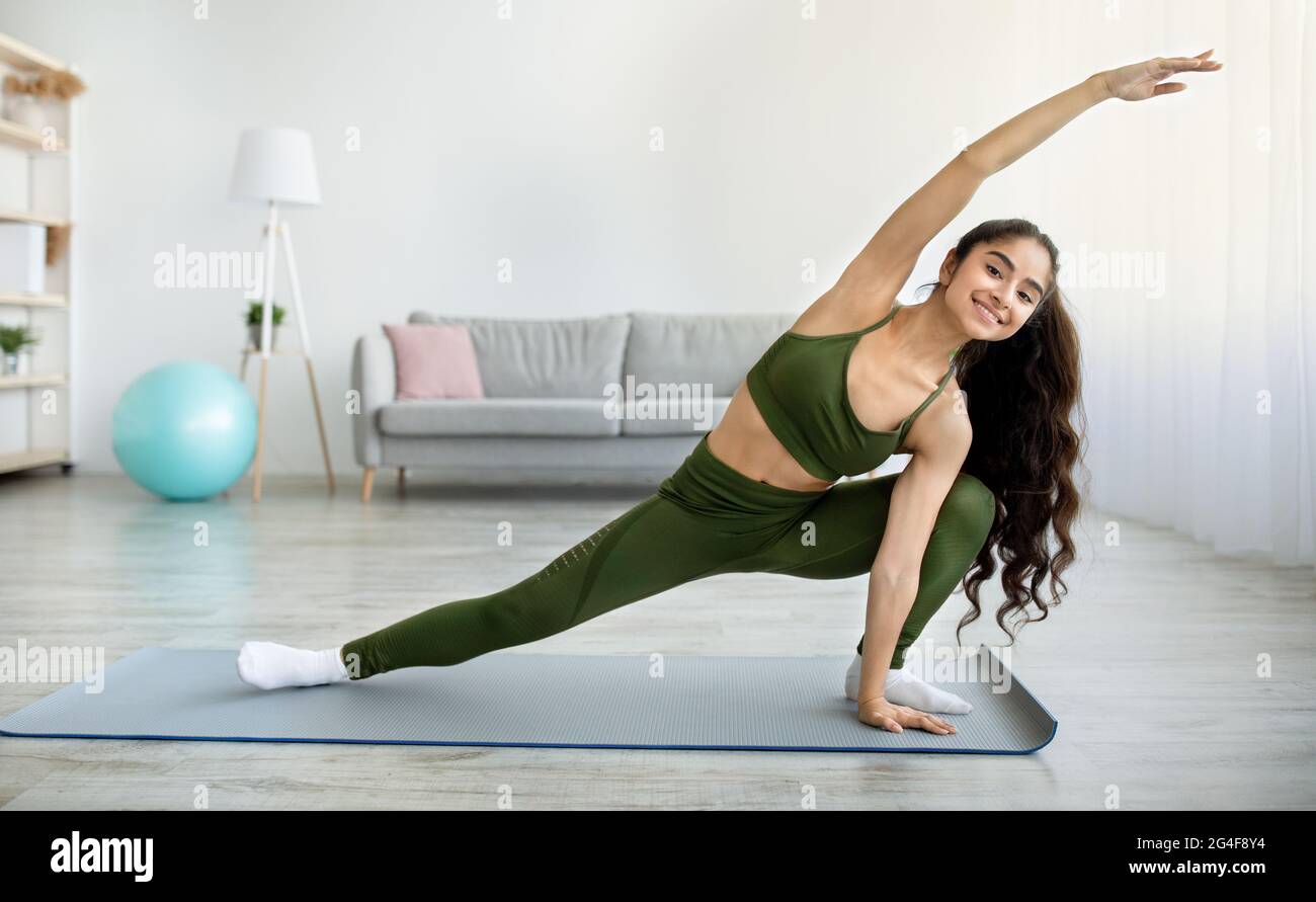 Junge Inderin praktiziert Yoga oder Pilates, dehnt Arme und Beine während des häuslichen Trainings, kopiert Raum Stockfoto