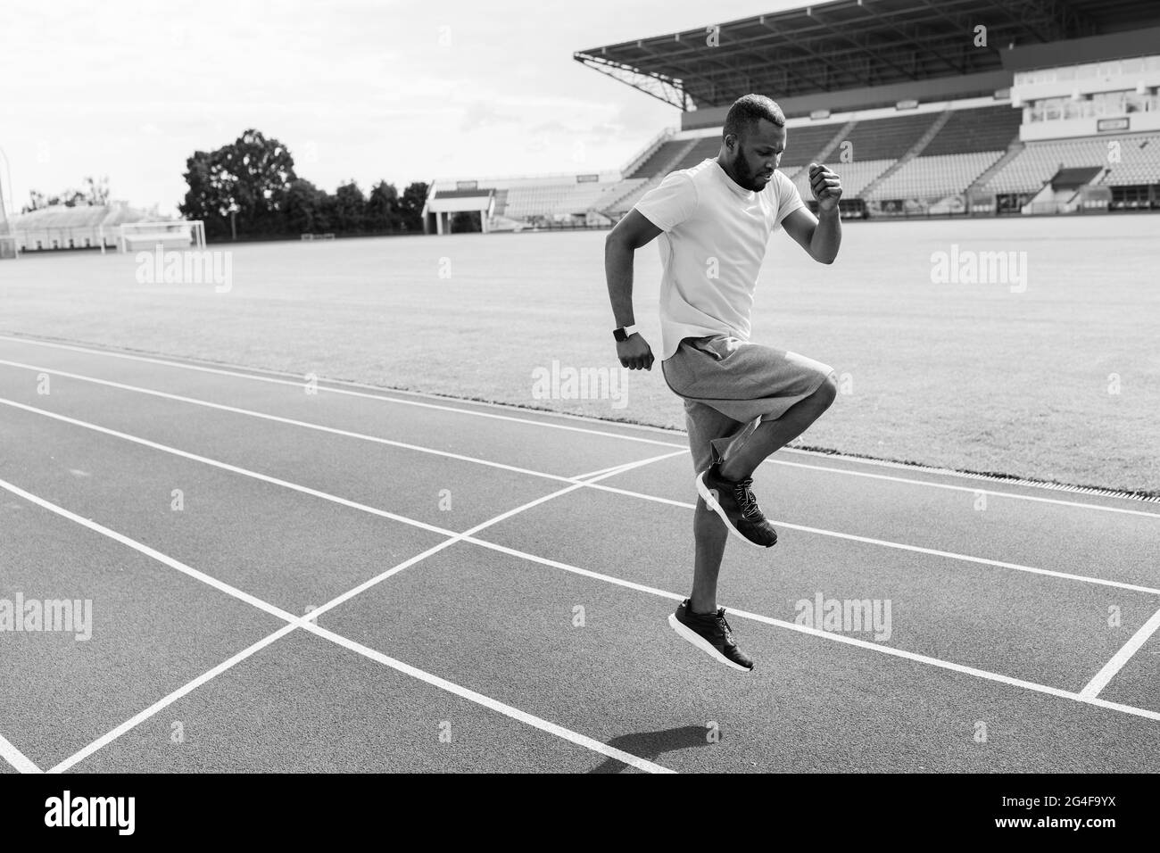 Schwarz-Weiß-Foto eines aktiven Mannes aus afroamerikanischem sport, der im Stadion Sportübungen macht. Junger fokussierter Mann, der sich auf ein wichtiges Spiel, Spiel vorbereitet Stockfoto