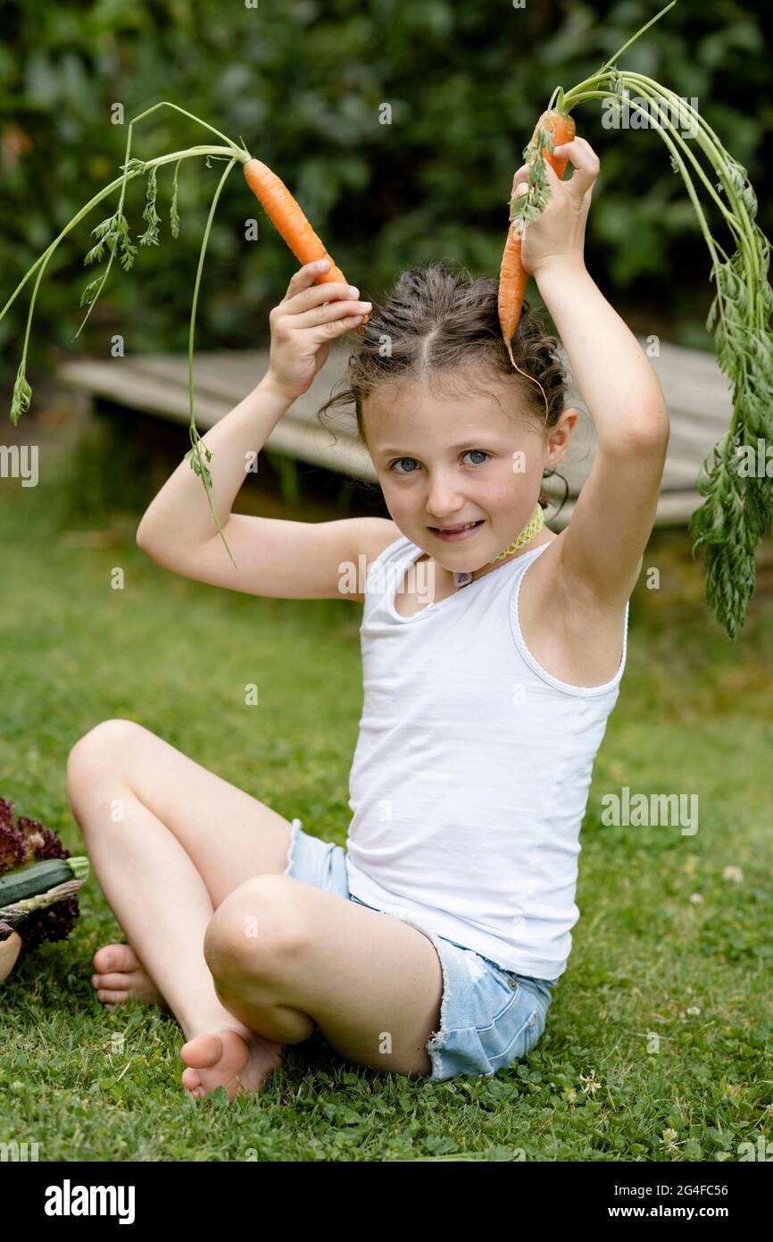 Mädchen sitzt auf der Wiese und zeigt Kaninchenohren mit Karotten Stockfoto