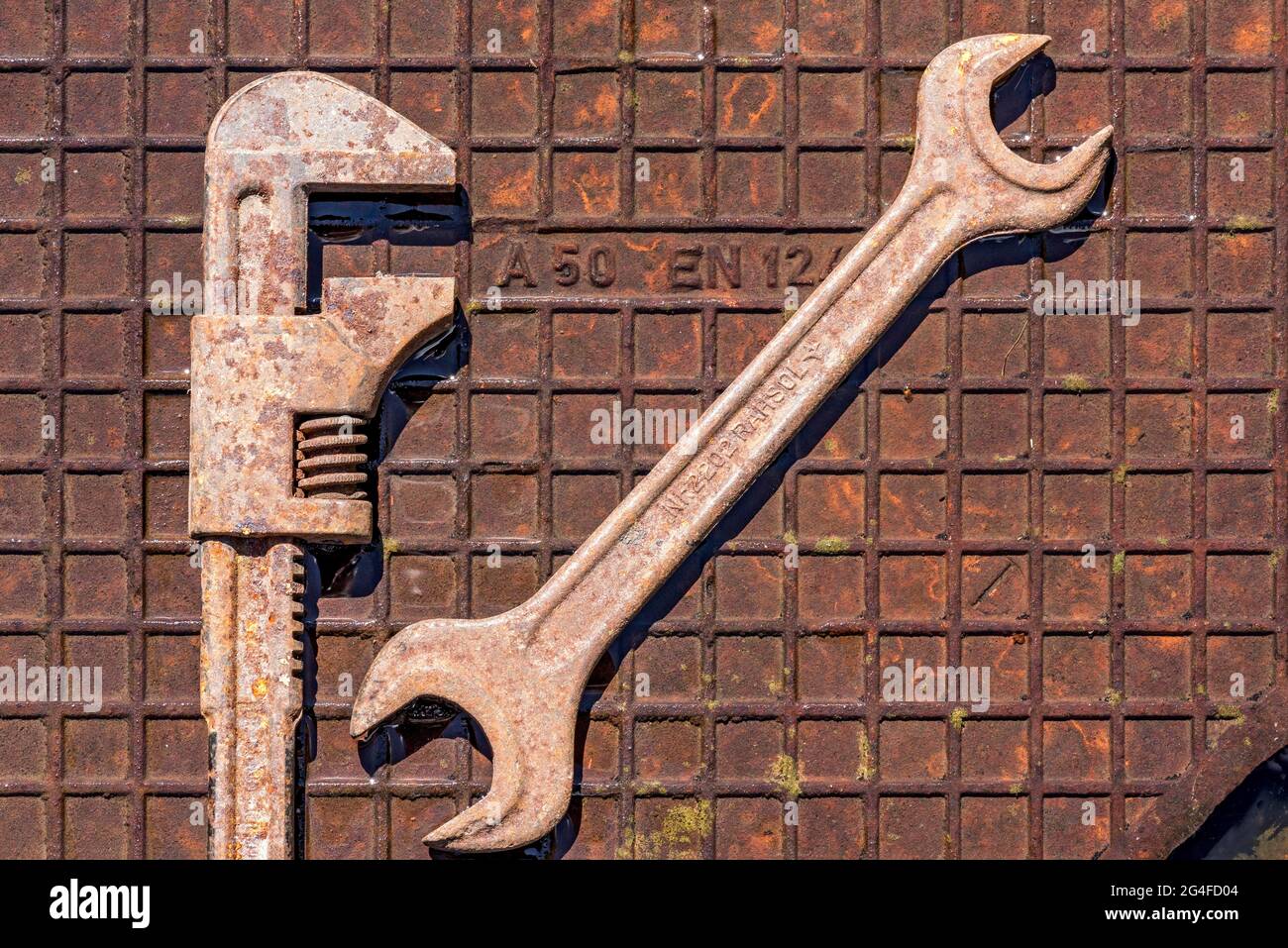 Alte Schraubenschlüssel, Rollgabelschlüssel oder Engländer, rostiges Werkzeug auf nasser rostiger Eisenplatte, Deutschland Stockfoto