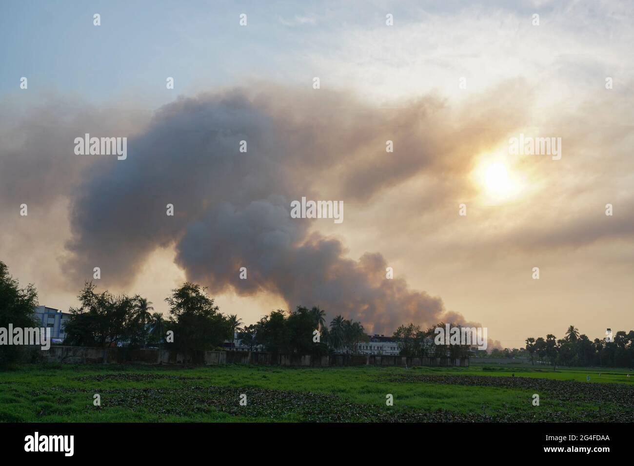 Rauch kommt aus Fabriken am Horizont, die Luftverschmutzung breitet sich wie Wolken aus und bedeckt die untergehende Sonne. Gedreht auf dem ländlichen Dorf WB, Indien. Stockfoto