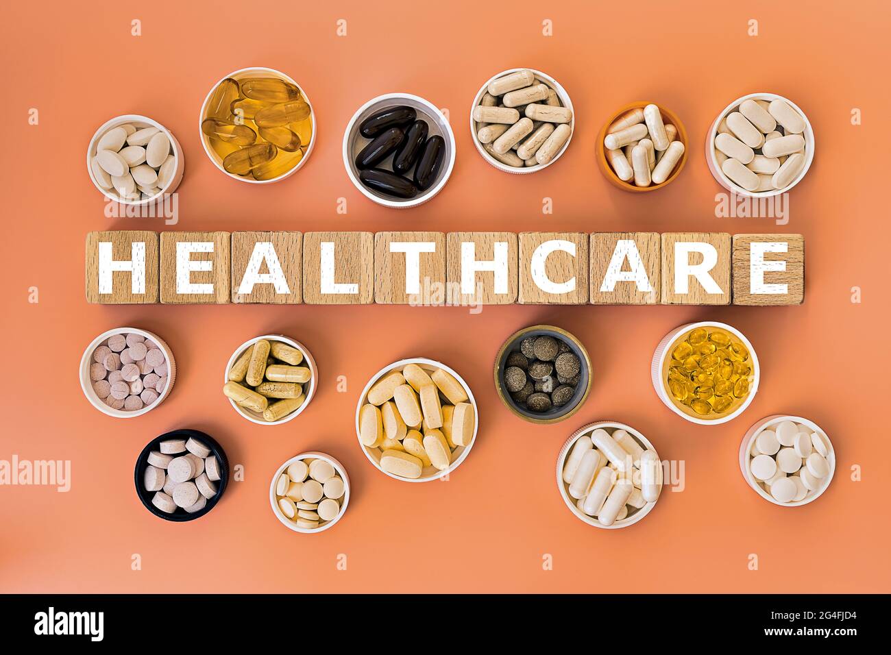 Foto zum Thema Gesundheit. Holzwürfel mit der Aufschrift „Gesundheit“ und biologisch aktive Nahrungsergänzungsmittel auf korallenfarbenem Hintergrund Stockfoto