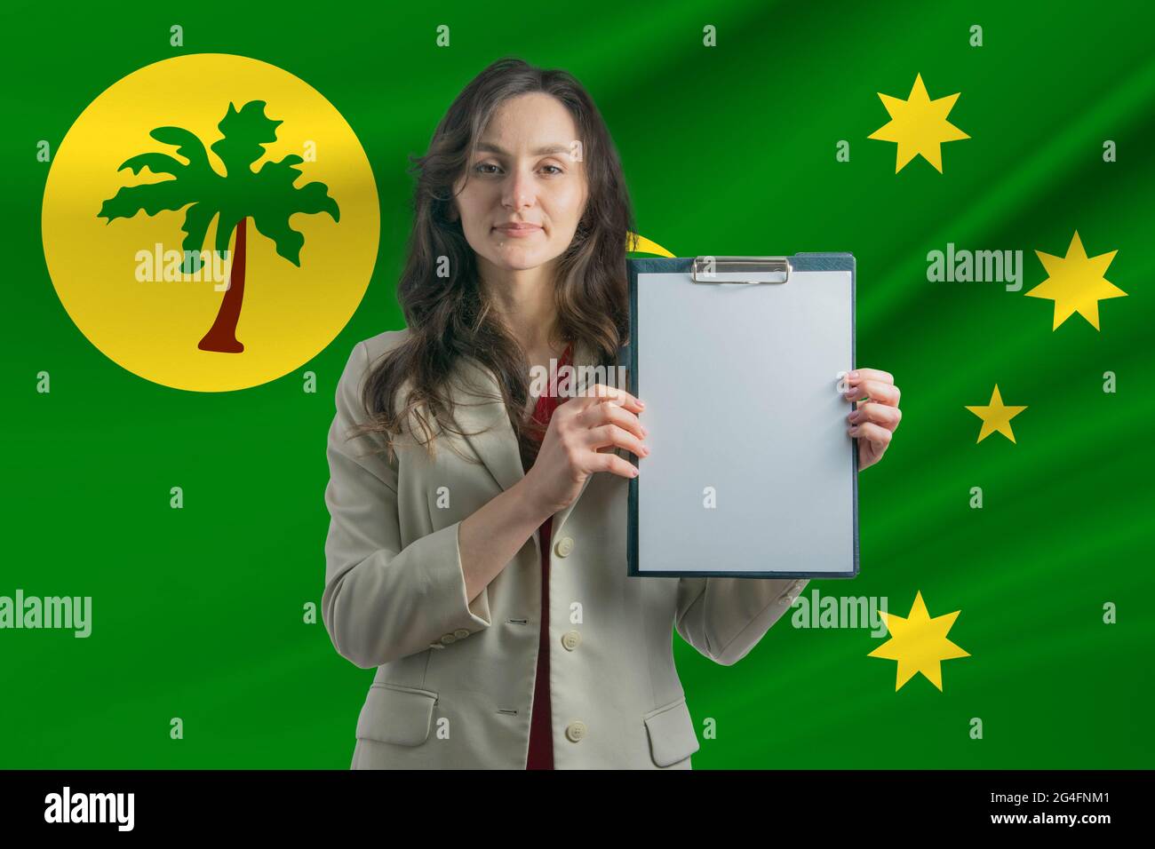 Studieren Sie auf Kokosinseln. Schöne Frau, die ein Blatt Papier in den Händen hält. Mädchen auf dem Hintergrund der Flagge der Kokosinseln. Stockfoto