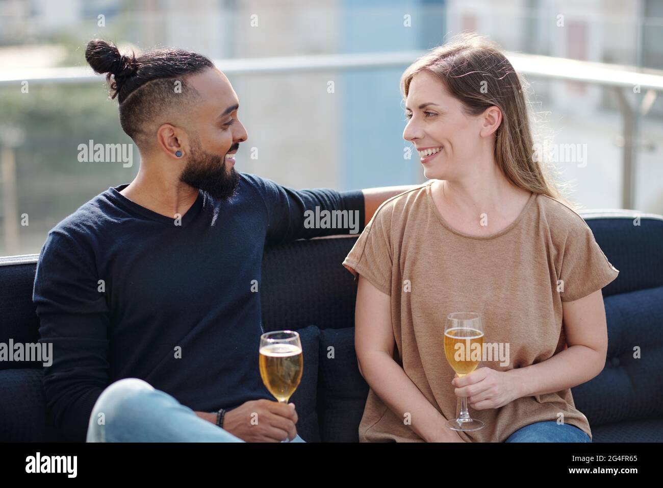 Lächelnder junger Mann und Frau trinken kalten Wein und reden auf der Dachparty Stockfoto