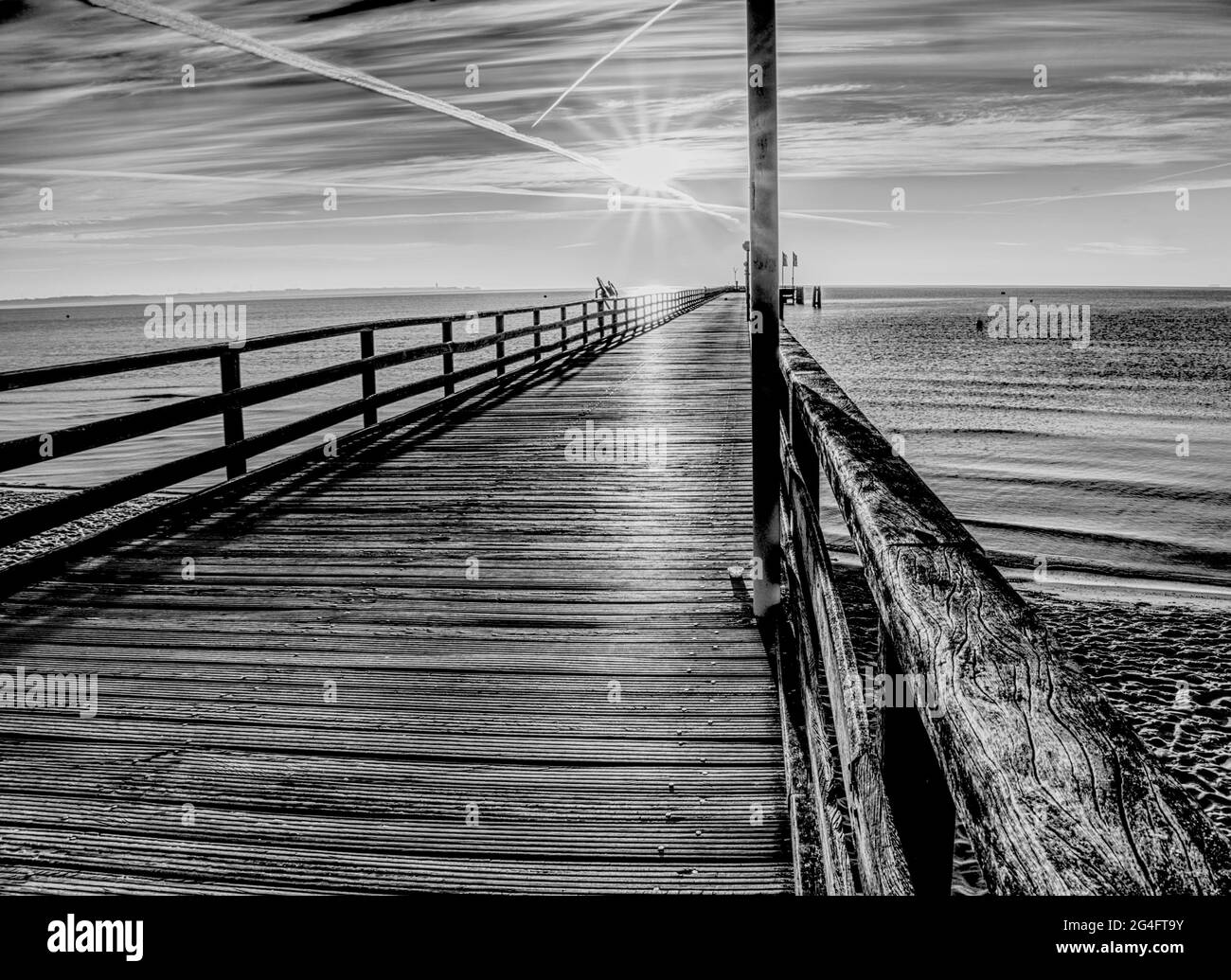 Blick in die Morgensonne über einen Pier, der in die deutsche Ostsee führt, abstrakt schwarz-weiß Stockfoto