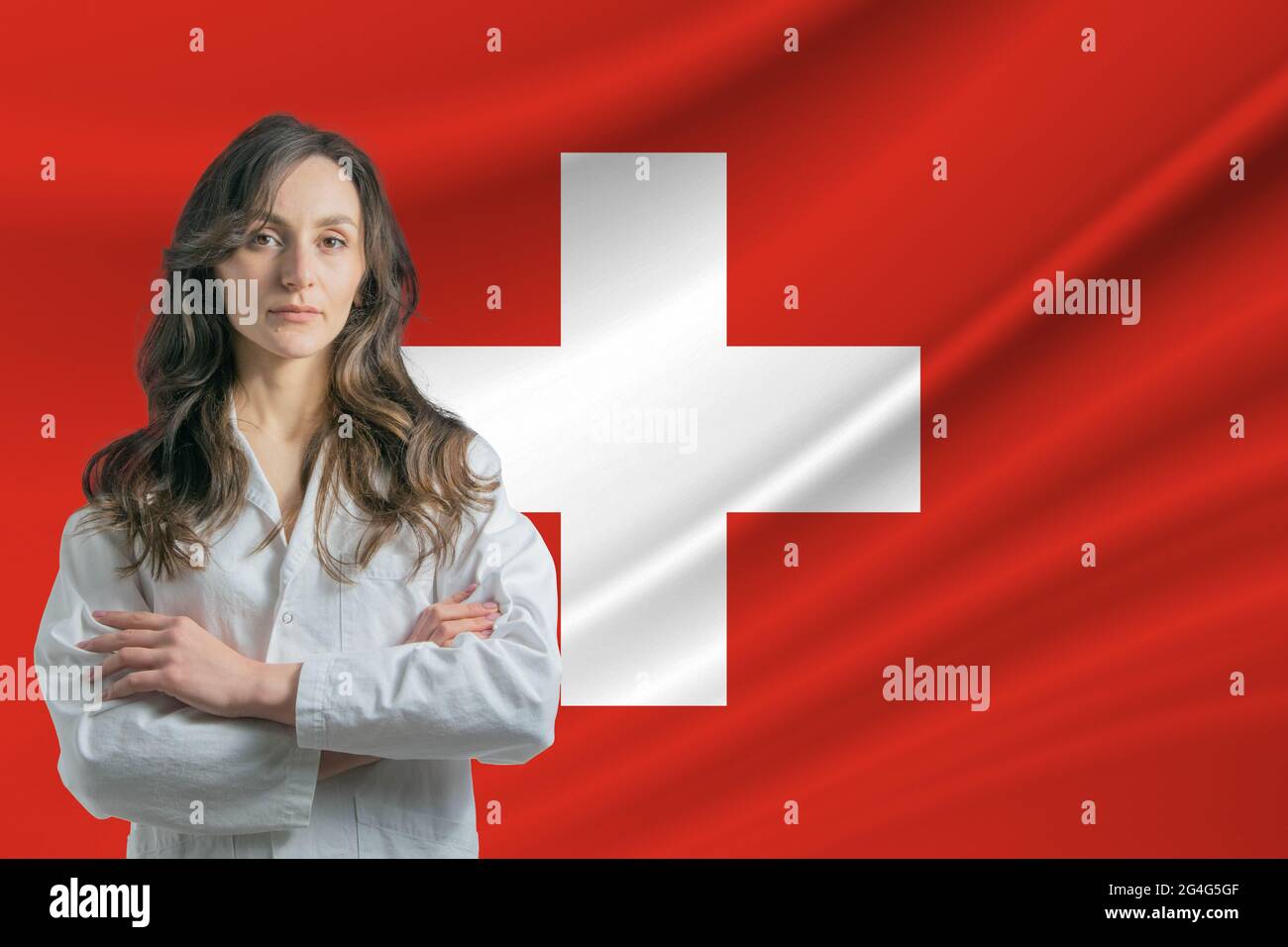 Medizin in der Schweiz. Fröhliche schöne Ärztin im medizinischen Mantel,  die mit gekreuzten Armen vor dem Hintergrund der Schweizer Flagge steht  Stockfotografie - Alamy