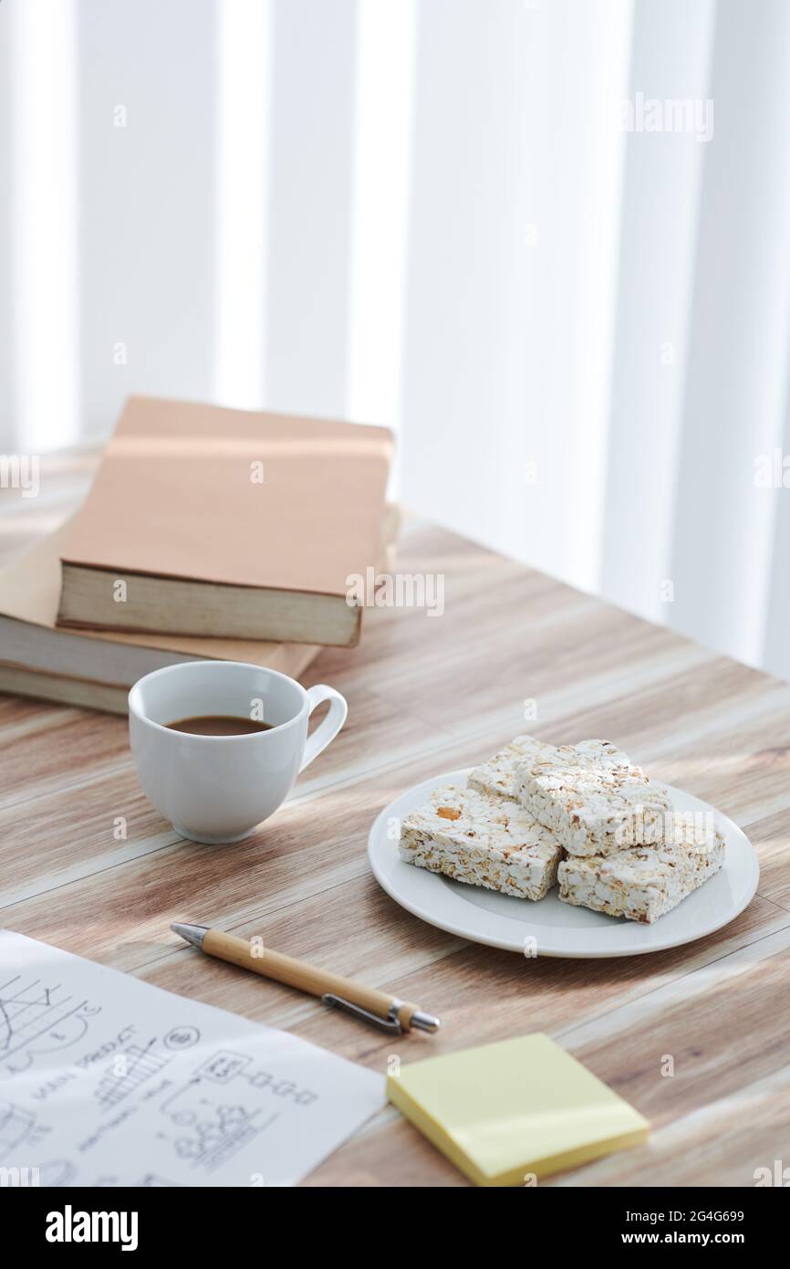 Eine Tasse Kaffee und Popcornbars auf dem Schreibtisch neben der Dokumentation mit Charts und Bücherstapel Stockfoto