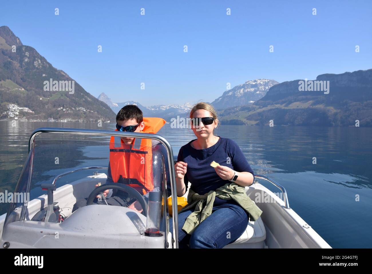 Mutter und Sohn picknicken auf einem Motorboot auf dem Vierwaldstättersee in der Schweiz. Der Junge trägt eine orangefarbene Schwimmweste und eine Sonnenbrille. Stockfoto