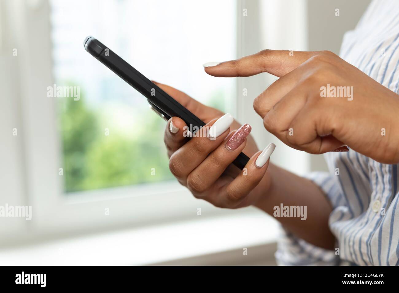 Die Hände einer afrikanischen Frau halten ein Mobiltelefon. Schwarze Studentin schreibt in einem Chat mit einem Smartphone. Nahaufnahme. Stockfoto