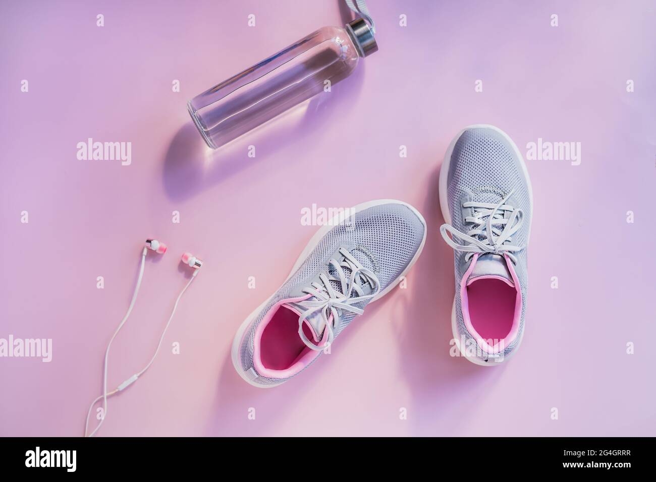 Turnschuhe, Kopfhörer und Wasserflasche aus Glas auf rosa Hintergrund. Set für Laufen und sportliche Aktivitäten. Gesunder und aktiver Lebensstil. Online Stockfoto