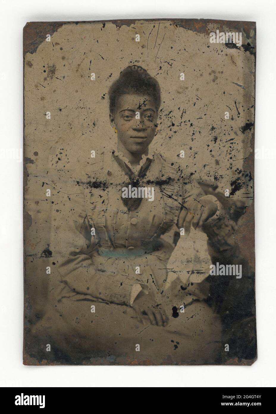 Eine nicht identifizierte afroamerikanische Frau, die ein langärmliges Kleid mit Spitzenkragen trägt. Die Platte ist getönt: Ihre Ohrringe und der Ring an ihrem linken Mittelfinger sind goldfarben gestrichen, ihre Wangen sind rosa und ihr Gürtel ist blaugrün bemalt. Sie hält ein Tuch in ihrer linken Hand und legt ihre andere Hand auf ihren Schoß. Stockfoto