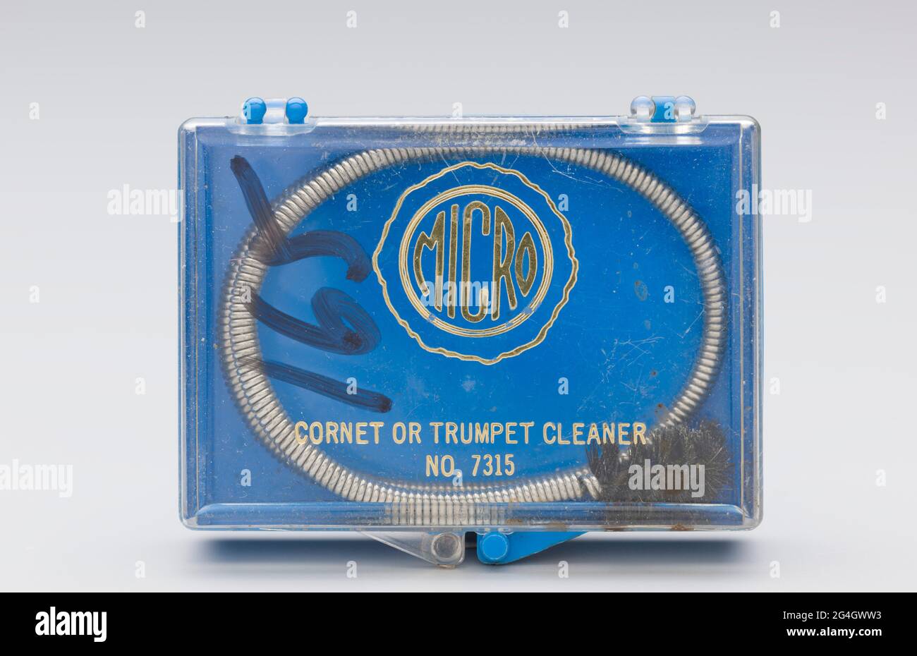 Ein Instrument, das Schlange und ihren Behälter reinigt. Die Reinigungsschlange (2013.46.29.1.3a) besteht aus flexiblem Federdraht mit einer schwarzen Nylonborstenbürste an einem Ende. Das Kunststoffgehäuse (2013.46.29.13b) für eine Reinigungsschlange. Das Gehäuse hat einen blauen Sockel und einen durchsichtigen, aufklappbaren Deckel, der vorne einrastet. Der goldene Text auf dem Deckel lautet: [MICRO / CORNET ODER TROMPETENREINIGER / NO. 7315]. Die Zahl [165] wurde in einem schwarzen Marker auf dem linken Drittel des Deckels angegeben. Stockfoto