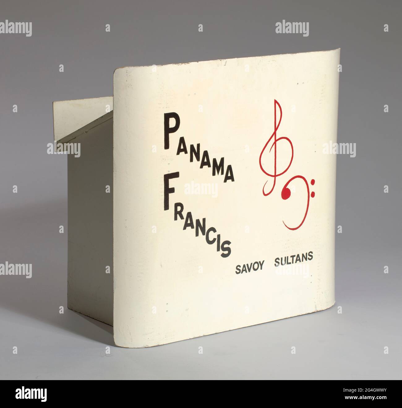 Panama Francis (1918-2001) war ein afroamerikanischer Swing-Jazz-Schlagzeuger, der in den 1950er Jahren auf zahlreichen Hit-Aufnahmen spielte. Ein klappbarer Musikständer. Es scheint aus Hartfaserplatten gefertigt zu sein, die mit einer glänzend weißen Farbe versehen sind, die das Aussehen von Metall verleiht. Es hat eine gebogene Frontplatte mit schwarzem Text, ein rotes Violinschlüssel-Symbol und ein rotes Bassschlüssel-Symbol, das von Hand bemalt erscheint. Der Text lautet [PANAMA / FRANCIS / SAVOY SULTANS]. An der Rückseite der Frontplatte sind vier (4) Klapptafeln angebracht, die beim Ausklappen einen offenen Kasten bilden. Die obere Abdeckung dient als Musikstütze. Es hat ein rundes Loch an der Spitze Stockfoto