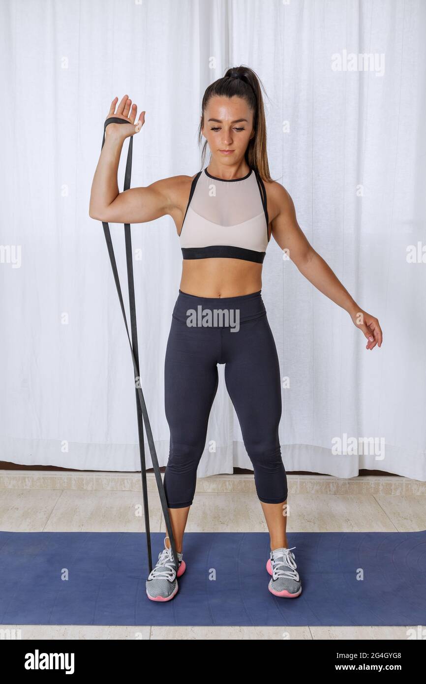 Ganzkörper von jungen fit weiblich in Sportbekleidung tun einen Arm Bicep Curl Übung mit Widerstand Seil während Fitness-Training zu Hause Stockfoto