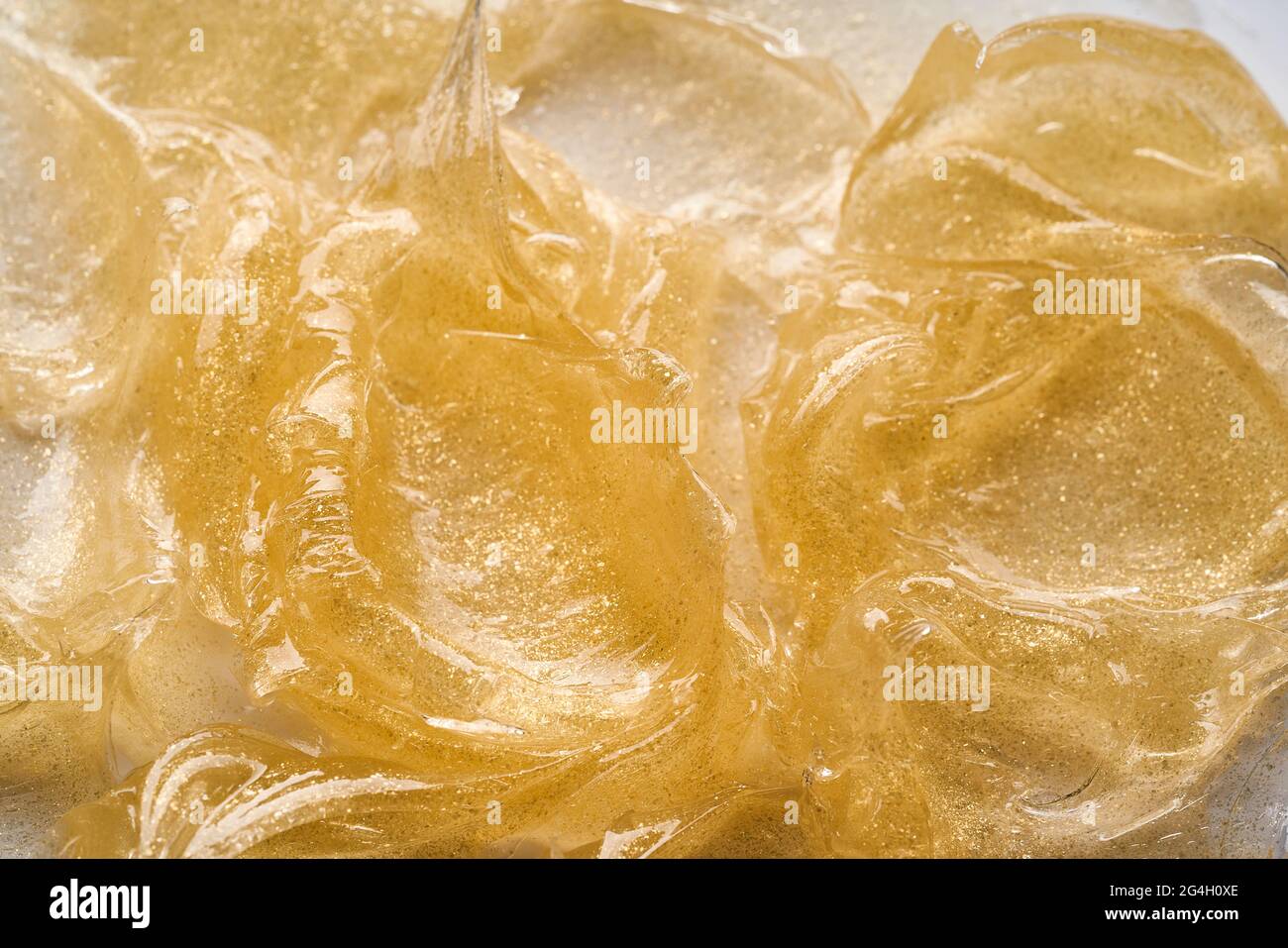 Transparenter Abstrich und Textur von goldenem Kosmetikgel auf weißem Hintergrund. Stockfoto