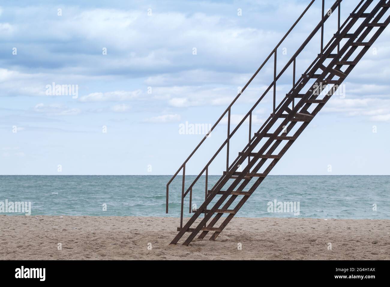 Die alte Metalltreppe geht am Sandstrand unter bewölktem Himmel hoch Stockfoto
