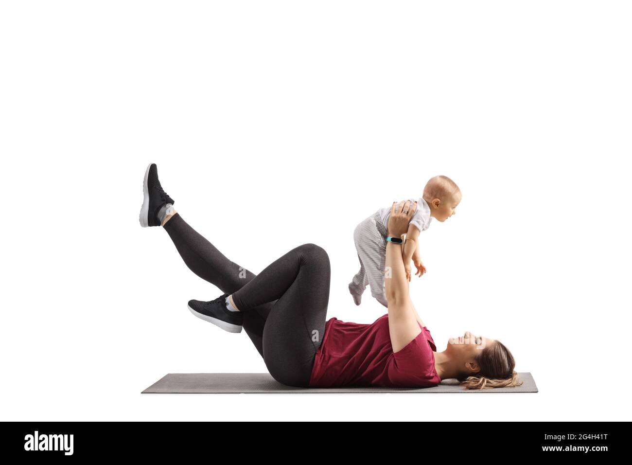 Junge Mutter, die auf einem Teppich liegt und mit ihrem Baby isoliert auf weißem Hintergrund trainiert Stockfoto