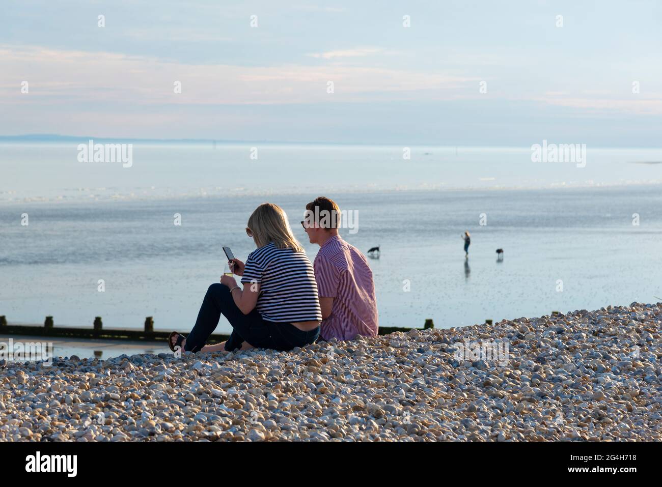 Das junge Paar sitzt am Strand von East Wittering und trinkt an einem warmen Abend im Mai ein Glas Wein mit der Isle of Wight am Horizont.West Sussex, England Stockfoto