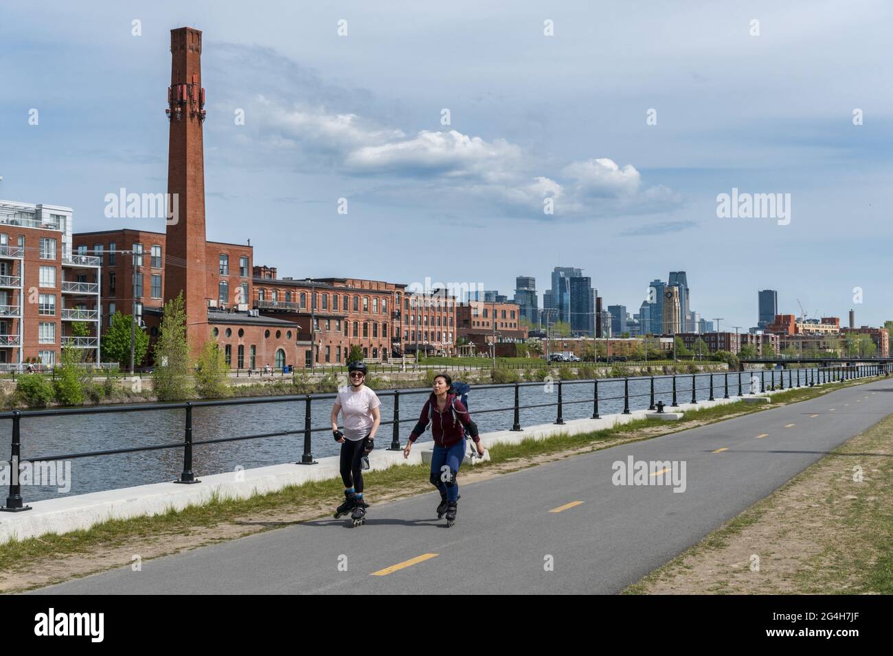 Montreal, CA - 15. Mai 2021: Schlittschuhlaufen auf dem Radweg des Lachine Canal, mit Skyline im Hintergrund. Stockfoto