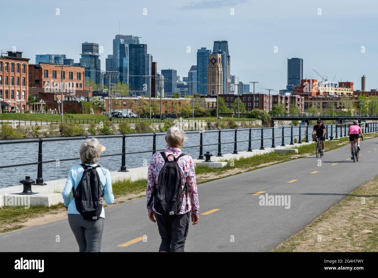 Montreal, CA - 15. Mai 2021: Menschen, die auf dem Radweg des Lachine Canal spazieren, mit Skyline im Hintergrund. Stockfoto