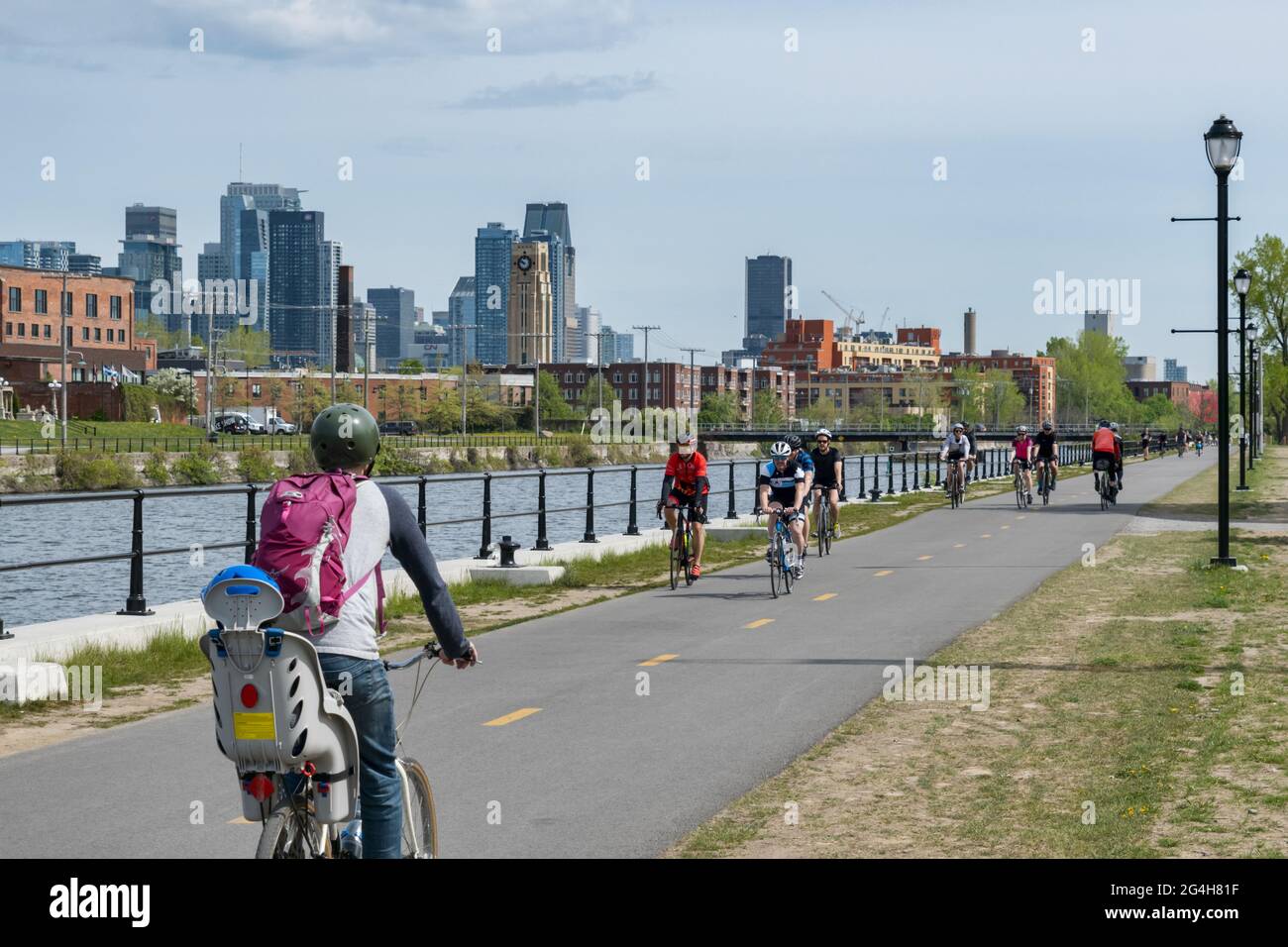 Montreal, CA - 15. Mai 2021: Menschen radeln auf dem Radweg des Lachine Canal, mit Skyline im Hintergrund. Stockfoto