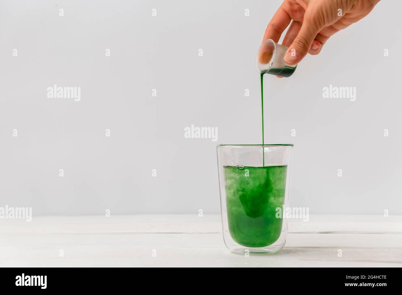 Frau gießt flüssiges Chlorophyll von Hand in einen Glasbecher. Weißer Hintergrund mit Platz für Text Stockfoto