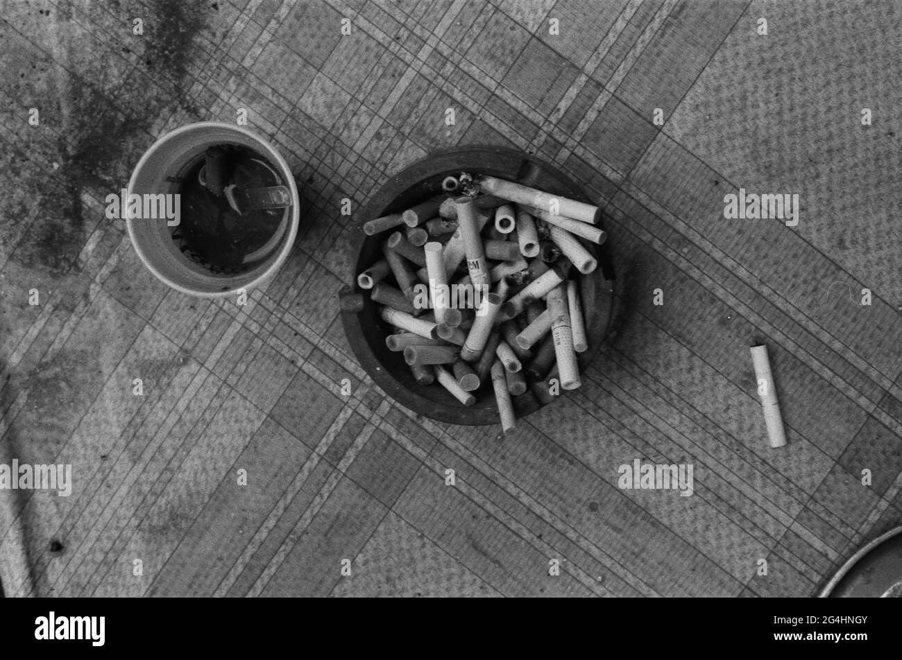 Aschenbecher voller Zigaretten auf Textur und Plastikbecher daneben gefüllt mit Zigaretten Stockfoto