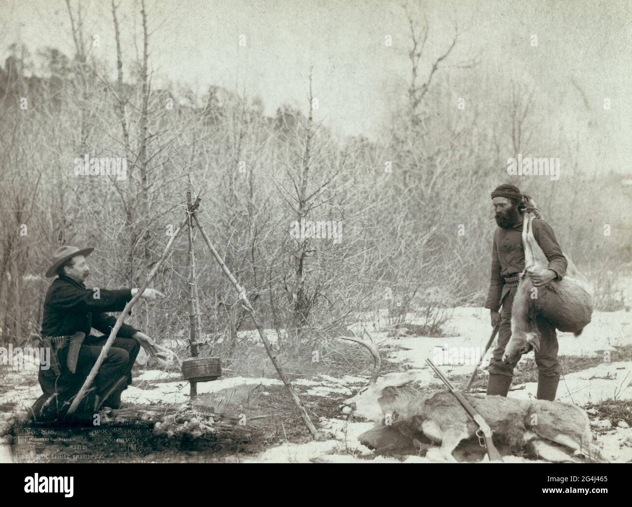 Jagd auf Hirsche - EINE Hirschjagd in der Nähe von Deadwood im Winter '87 und '88. Zwei Bergmänner McMillan und Hubbard haben ihr Spiel bekommen - zwei Jäger am Lagerfeuer; einer kocht, der andere hält einen toten Hirsch über seine Schulter Stockfoto