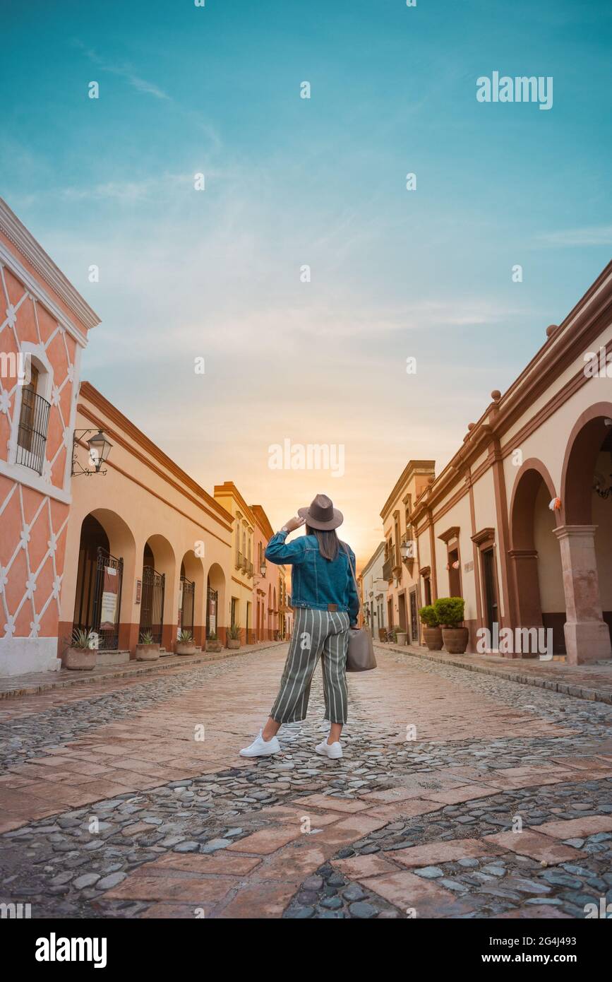 Tourist Frau, die in der Mitte der Straße einer magischen Stadt, Stadt La Peña del Bernal in Querétaro, Mexiko, mit Sonnenuntergang vor, Sommer da Stockfoto