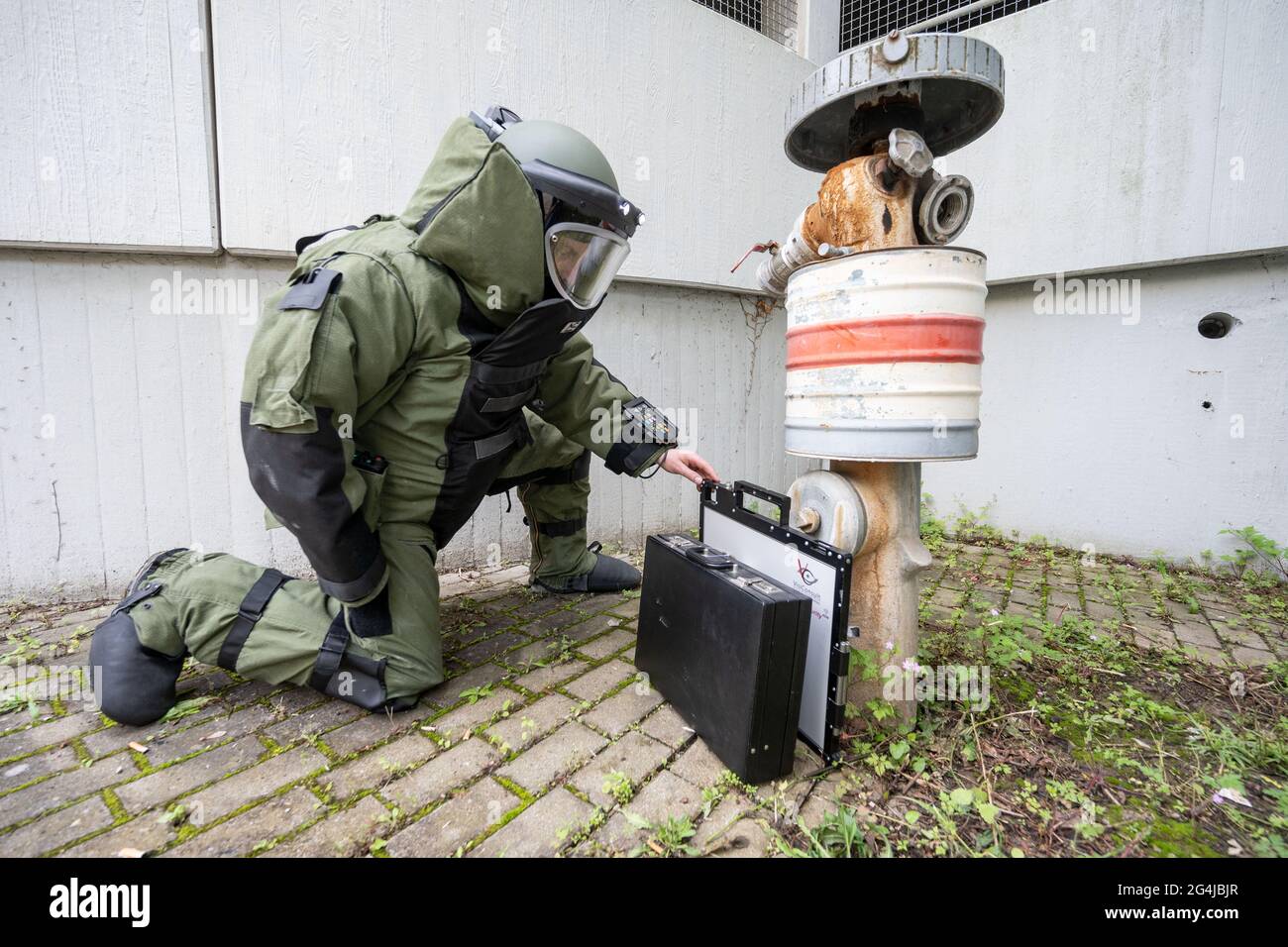 Stuttgart, Deutschland. Juni 2021. Bei einer Demonstration einer Übung des Landeskriminalamtes Baden-Württemberg legt ein entschärfender Offizier in einem Bombenschutzanzug eine Rötungsplatte für ein mobiles Röntgengerät vor einen an einen Hydranten gelehnten Koffer. (To dpa: 'Defusers of the LKA - Manchmal sprengen sie sich selbst') Quelle: Marijan Murat/dpa/Alamy Live News Stockfoto