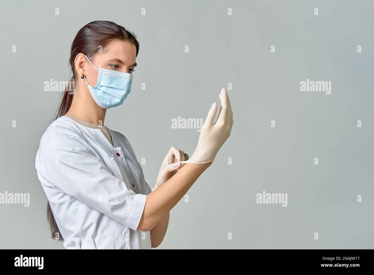 Ein Arzt in einem weißen Mantel und einer medizinischen Maske legt sterile weiße Latexhandschuhe auf seine Hände für den Eingriff, Kopierraum Stockfoto