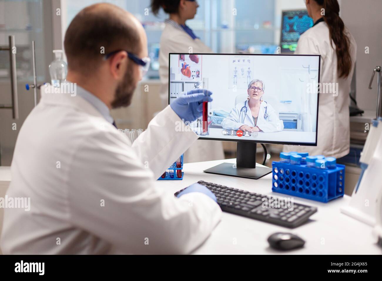 Reseacher hält Blutprobe und spricht während eines virtuellen Videoanrufs mit dem Arzt über die Behandlung. Wissenschaftler untersuchen die Entwicklung von Impfstoffen mithilfe von Hightech-Forschung in den Bereichen Behandlung, Gesundheitsinnovation und Mitarbeiterkollaboration. Stockfoto