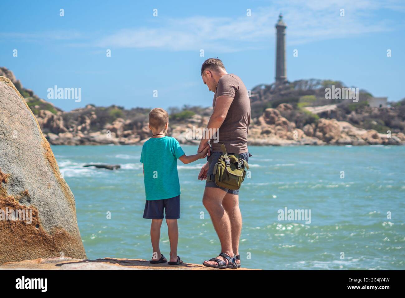 Dad Care Sohn in der Nähe des Meeres, Spaziergang Verbringen Sie Zeit zusammen, um Neues zu entdecken. Mann hält die Hand des Kindes. Leuchtturm Hintergrund Symbol des individuellen Bewusstseins, Aufzucht Junge Stockfoto