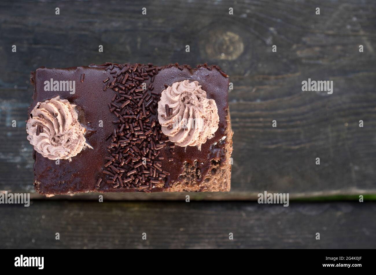 Mit Schokoladenstreuseln bestäubter, geschichteter Kuchen mit Schokocreme-Schüssen. Gebäck auf dunklem Holzhintergrund Stockfoto