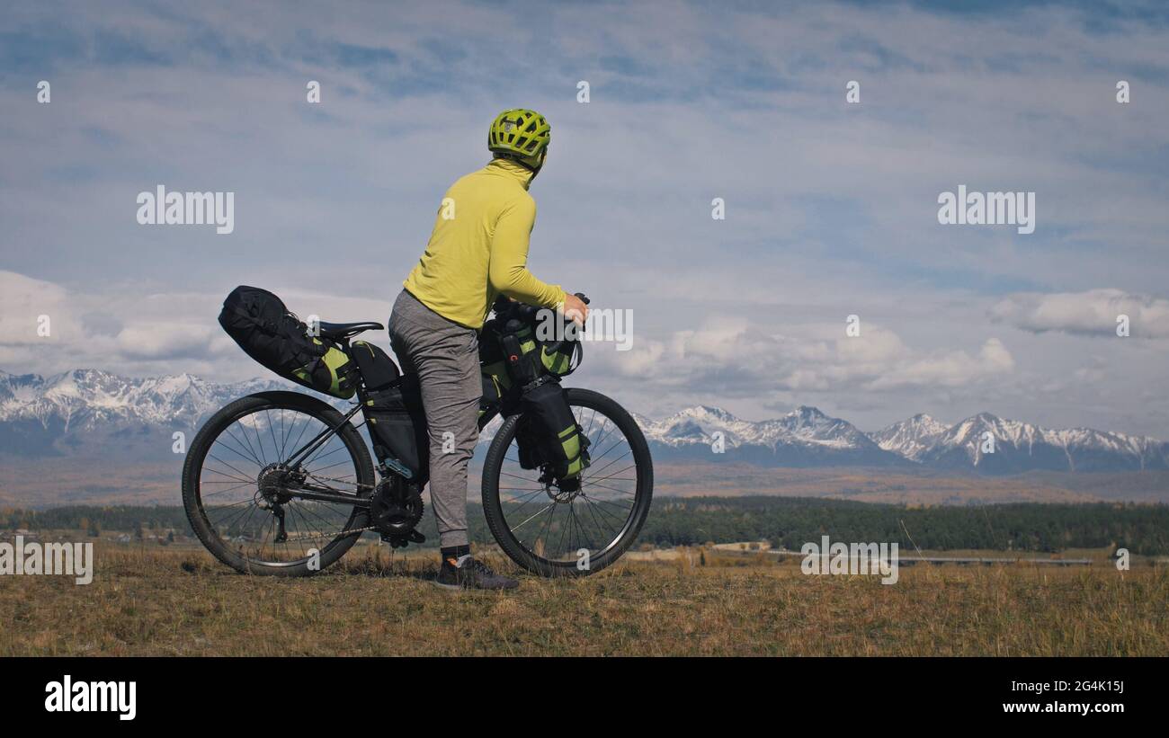 Der Mann und die Frau reisen auf gemischtem Terrain mit Bikepacking. Die beiden Personen reisen mit Fahrradtaschen. Schneebedeckte Berge. Stockfoto