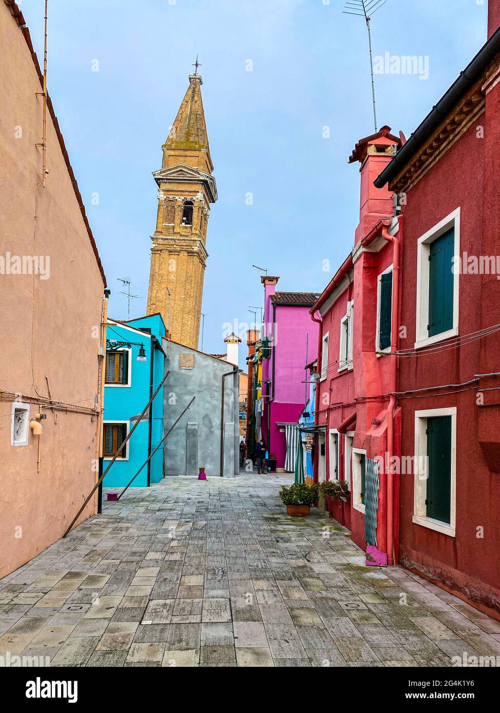 Farbenfrohe Häuser in einer kleinen traditionellen Straße mit der Spitze einer Kirche auf der Insel Burano, Venedig, Italien Stockfoto