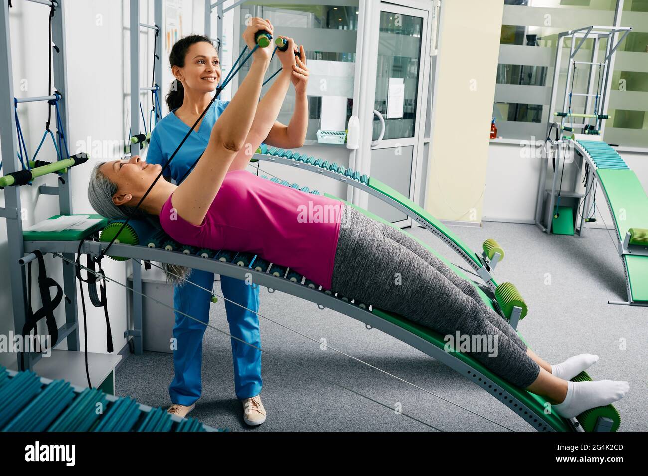 Die Physiotherapeutin unterstützt eine Patientin bei der Rücken- und Rückenrehabilitation und stellt sie mit einem speziellen Rehabilitationstrainer im Reha-Raum wieder her Stockfoto