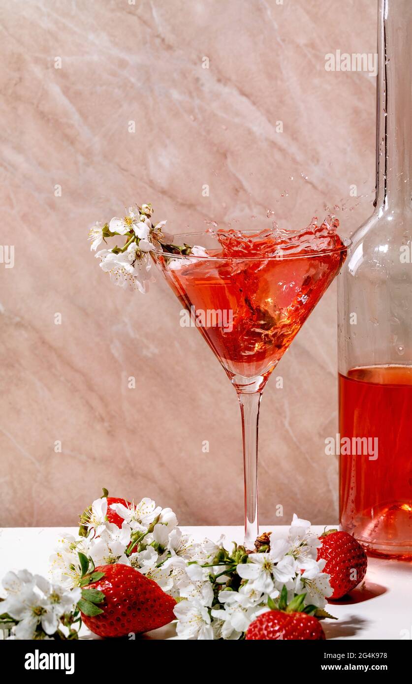 Spritzer alkoholischer oder alkoholfreier Erdbeercocktail in martiniglas- und Glasflasche, verziert mit blühenden Ästen von Kirschbäumen über weißem A Stockfoto