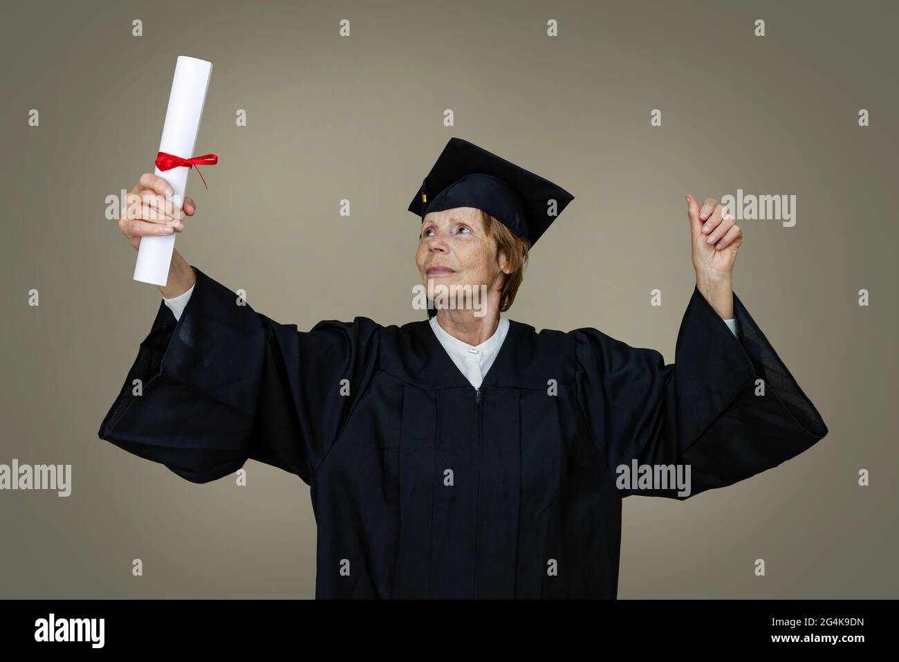 Stolze ältere Frau Absolventin in Abschlusskleid und Mütze mit Hochschuldiplom Stockfoto