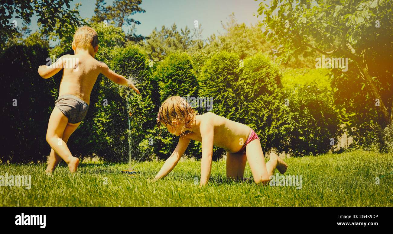 Kinder, die am heißen Sommertag im Garten mit Rasensprenger spielen Stockfoto