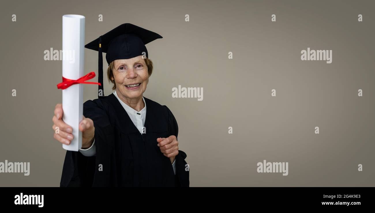 Seniorenausbildung - reife Absolventin Frau in Abschlusskleid und Kappe zeigt Diplom. Copy space Stockfoto