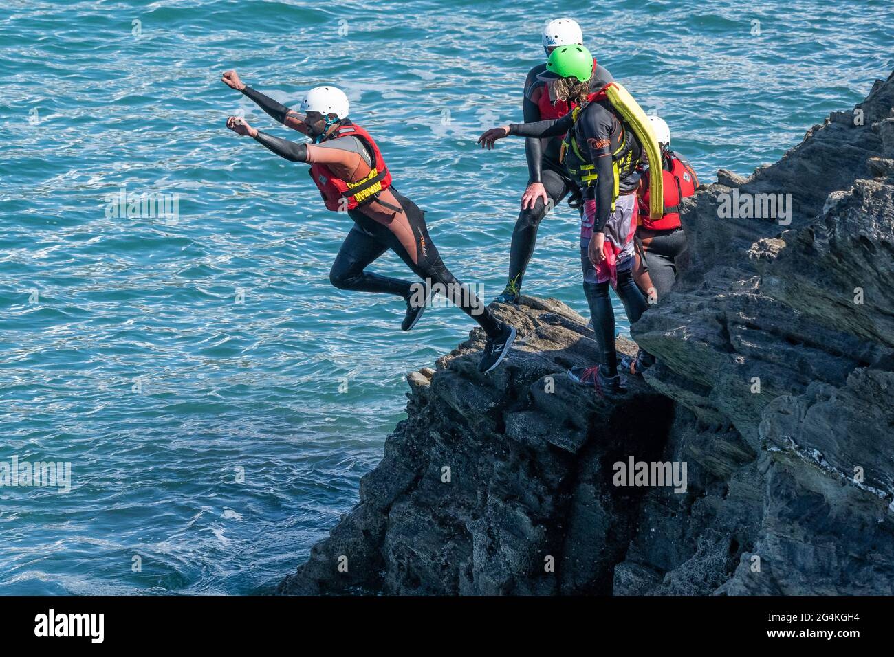 Urlauber, die von Felsen springen und mit einem Fremdenführer auf Towan Head in Newquay in Cornwall herumlaufen. Stockfoto