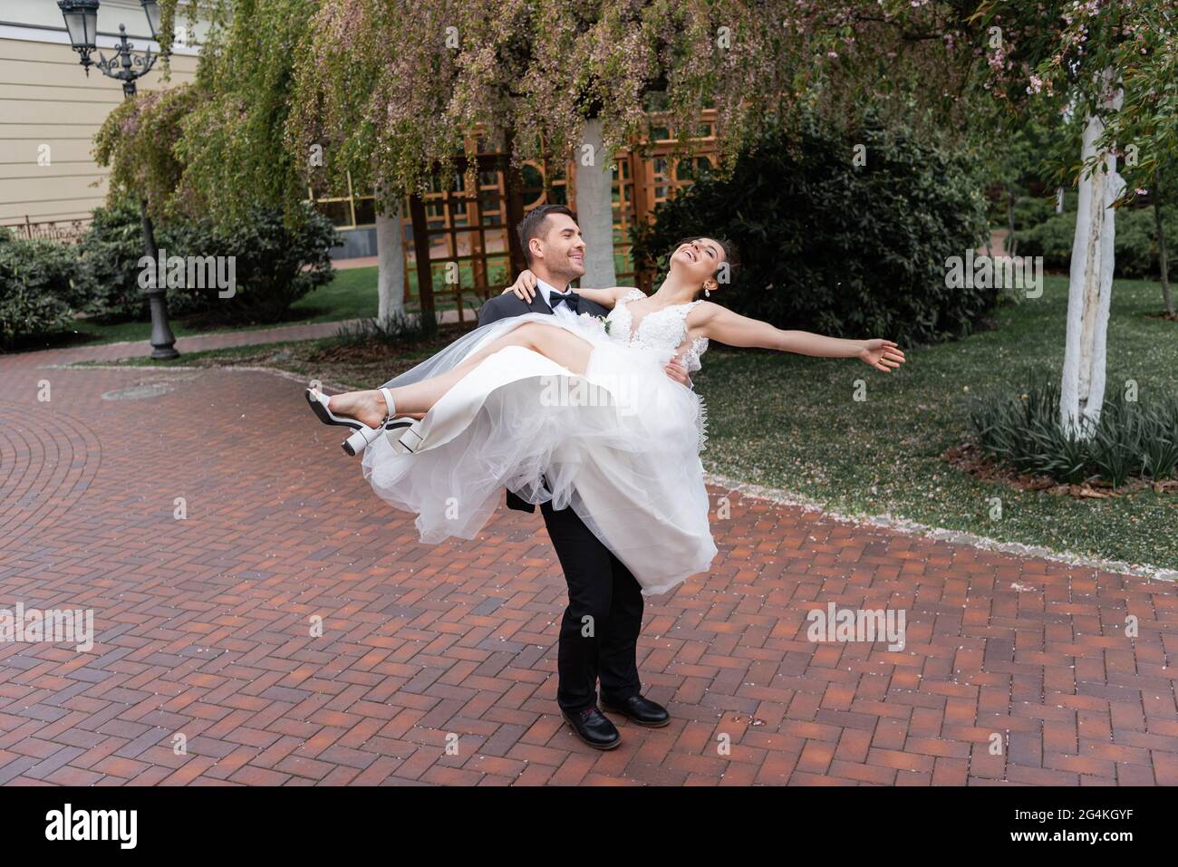 Happy Groom Spinning Braut in weißem Hochzeitskleid im Park Stockfoto