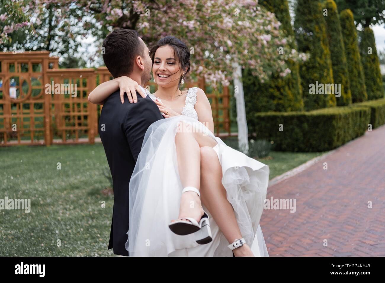 Bräutigam hält an den Händen lächelnde Braut in weißem Hochzeitskleid im Park Stockfoto