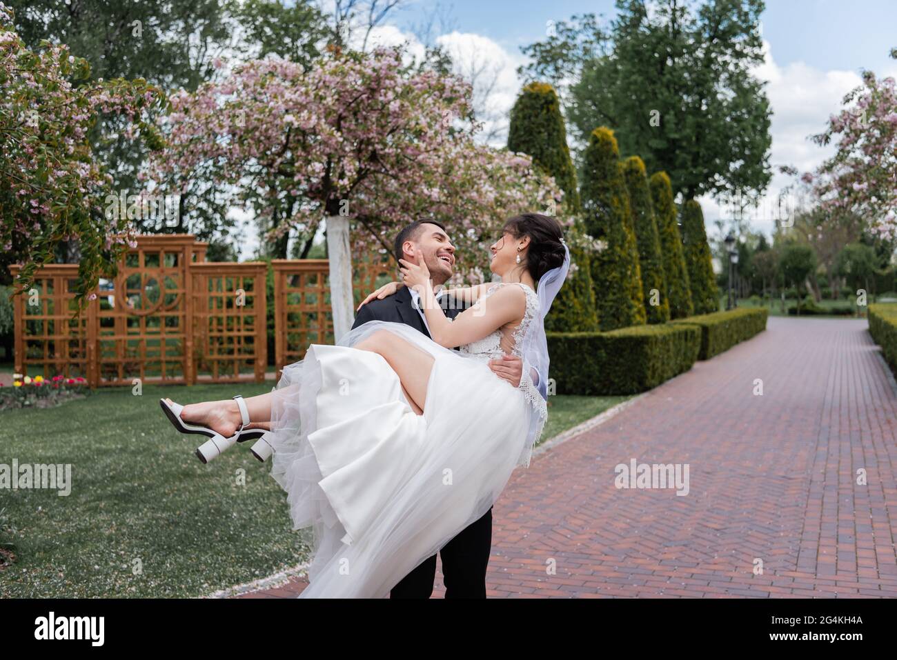Fröhlicher Bräutigam hält die Braut im Hochzeitskleid im Park an den Händen Stockfoto
