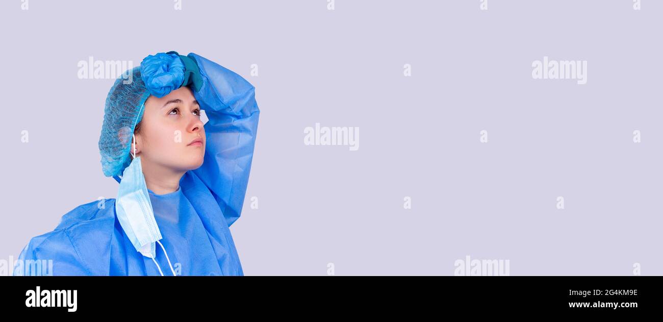 Banner, Langformat. Junge Ärztin ist es leid zu arbeiten. Grauer Hintergrund. Sie trägt blaue Uniform. Stockfoto