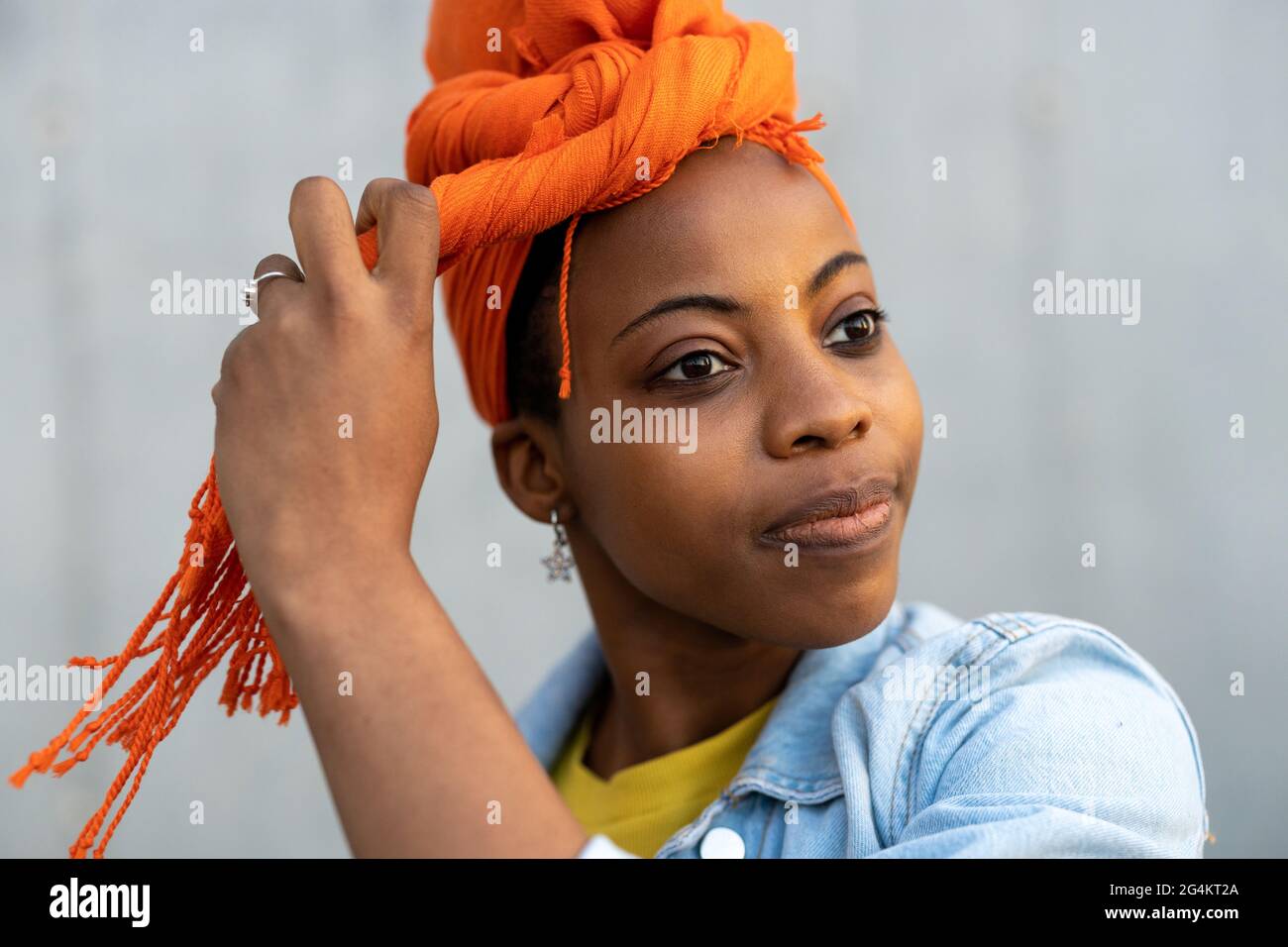 Junge Frau mit orangefarbenem Kopftuch vor der grauen Wand Stockfoto