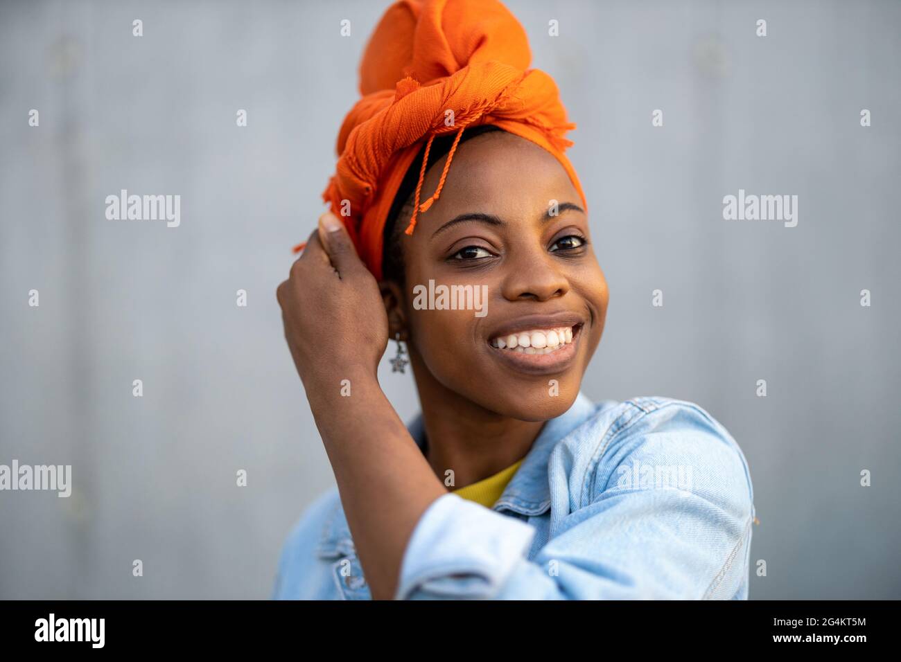 Junge Frau mit orangefarbenem Kopftuch vor der grauen Wand Stockfoto